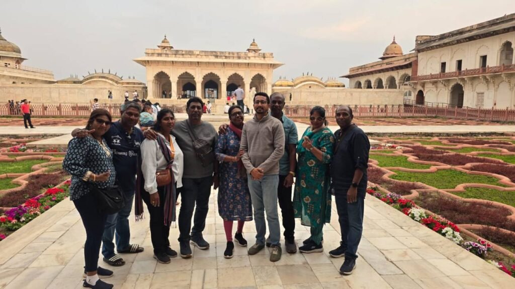 Eight tourists standing together at Angoori Bagh inside Agra Fort, with Jahangir Mahal Mughal architecture in the background during a guided tour by Agra Trip Packages.