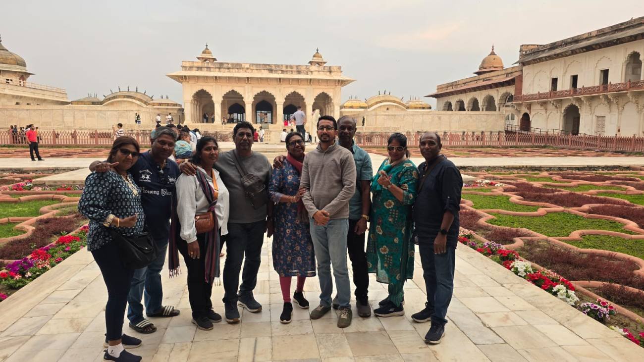 Safety and Comfort 4 Eight tourists standing together at Angoori Bagh inside Agra Fort, with Jahangir Mahal Mughal architecture in the background during a guided tour by Agra Trip Packages.