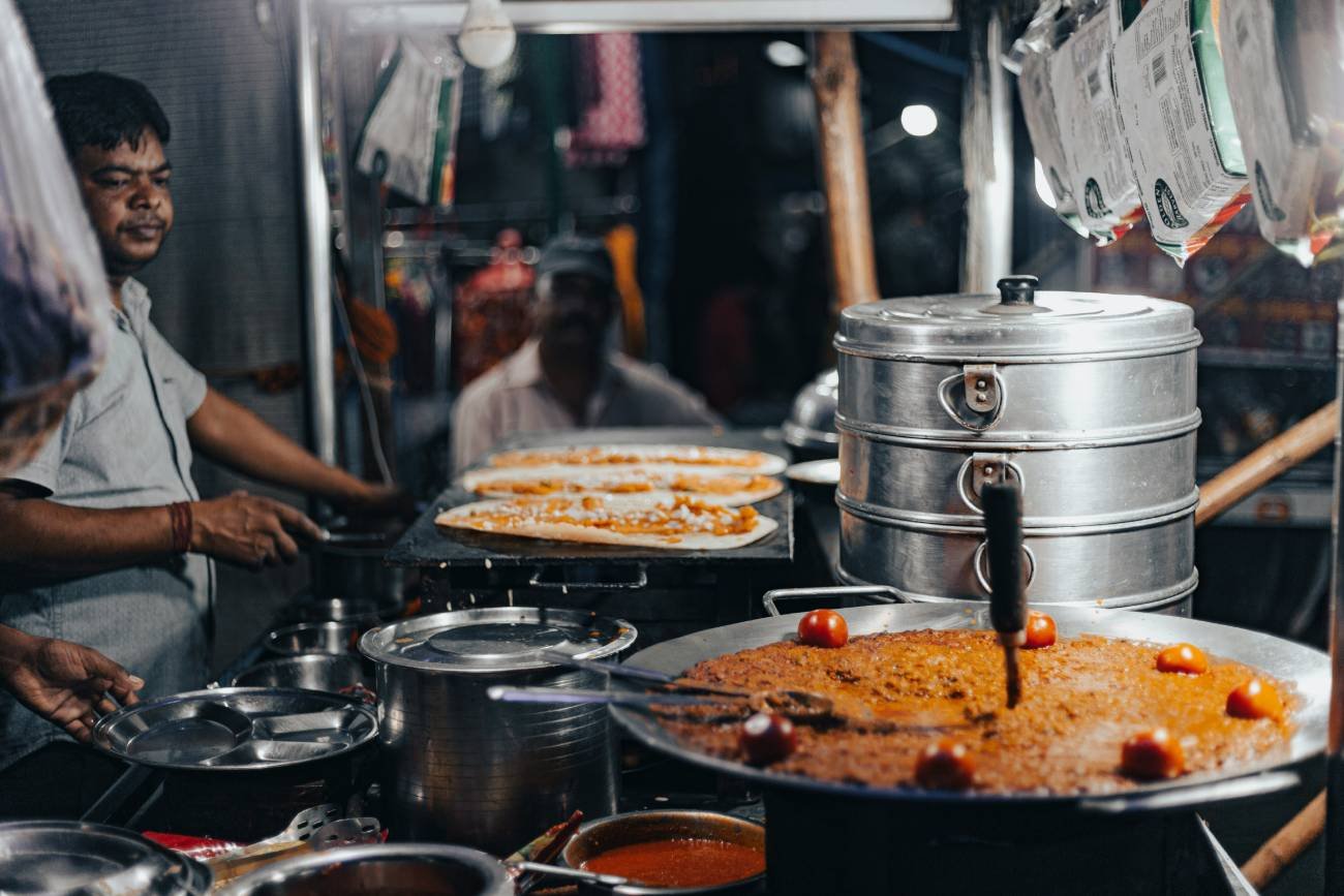 Welcome to Agra Trip Packages - A Government-Certified Travel Agency in Agra 165 Street food vendor cooking traditional Indian food at a busy local market stall in Agra with large cooking pots, fresh flatbreads, and authentic evening food scene.